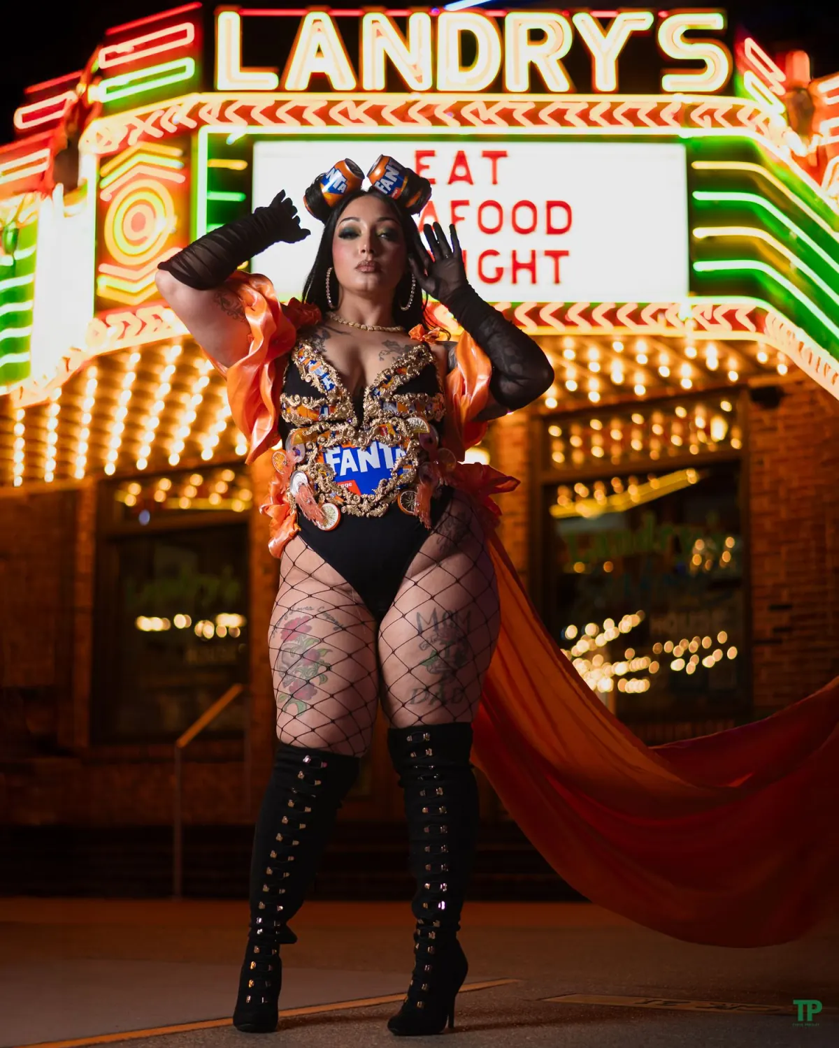 Woman in an orange and black outfit posing beneath a neon marquee at night